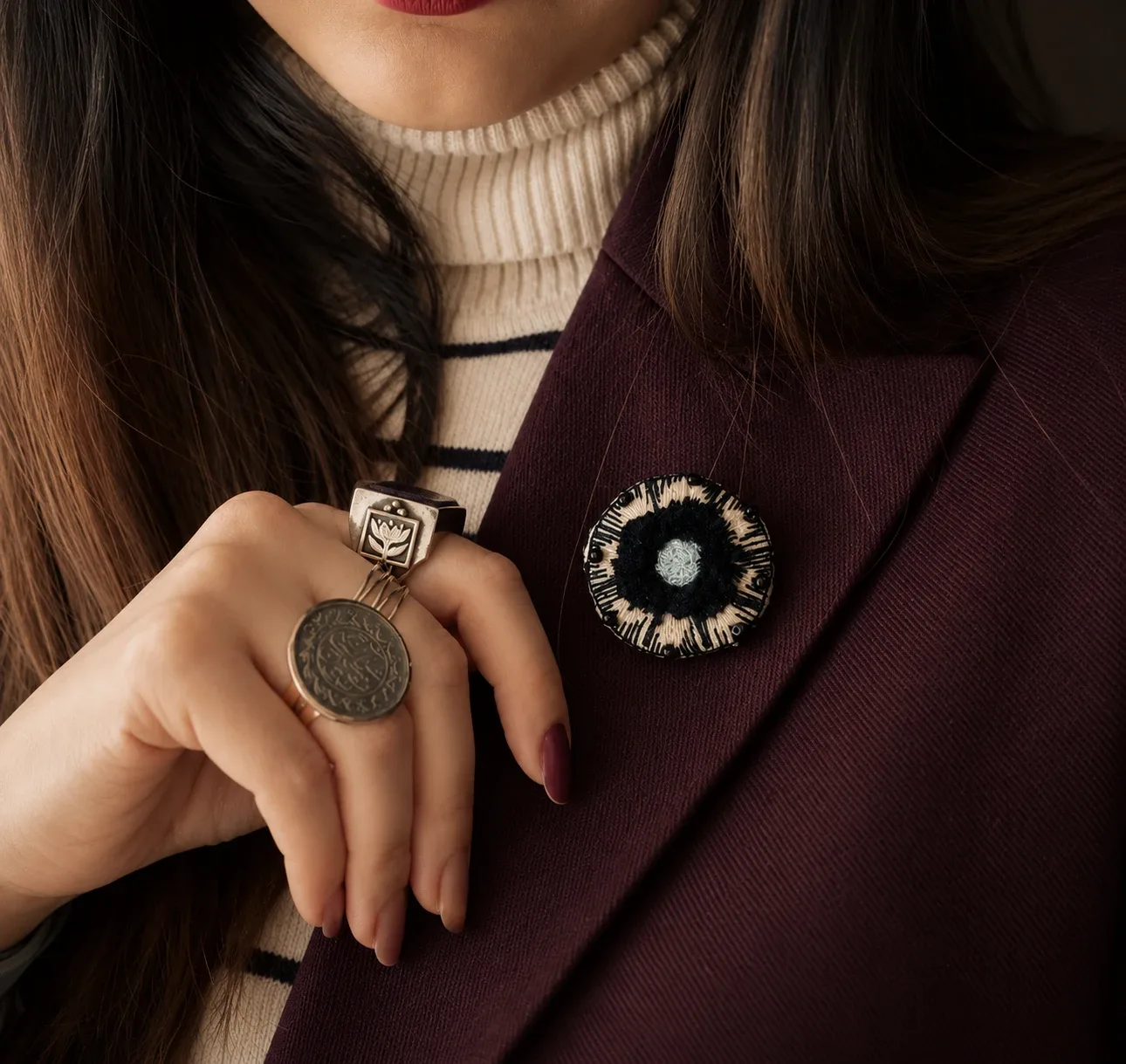 Round black, cream and pale blue embroidered brooch worn on a plum jacket lapel